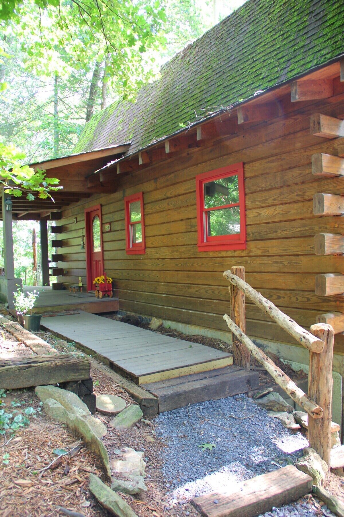 A wooden cabin with a porch, red-framed windows, and a wooden staircase leading to the entrance.