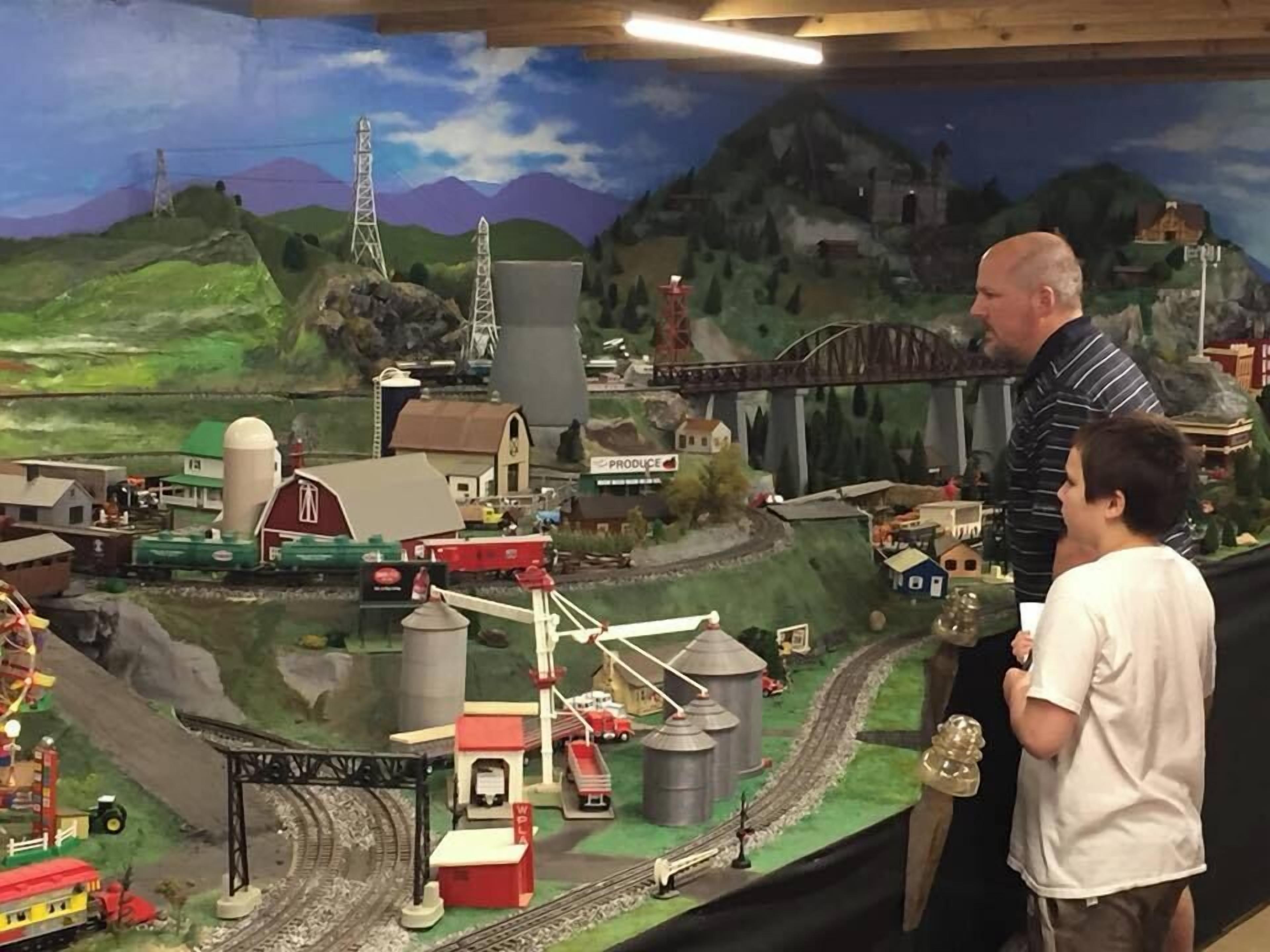 Un plastico ferroviario con un ponte, edifici e uno sfondo montuoso.