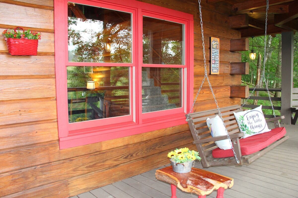 A wooden cabin with a porch, a swing, and a bench with cushions.