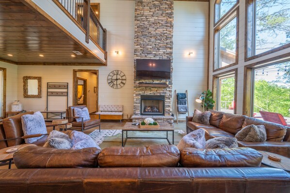 A spacious living room with leather sofas, a stone fireplace, and a large TV.