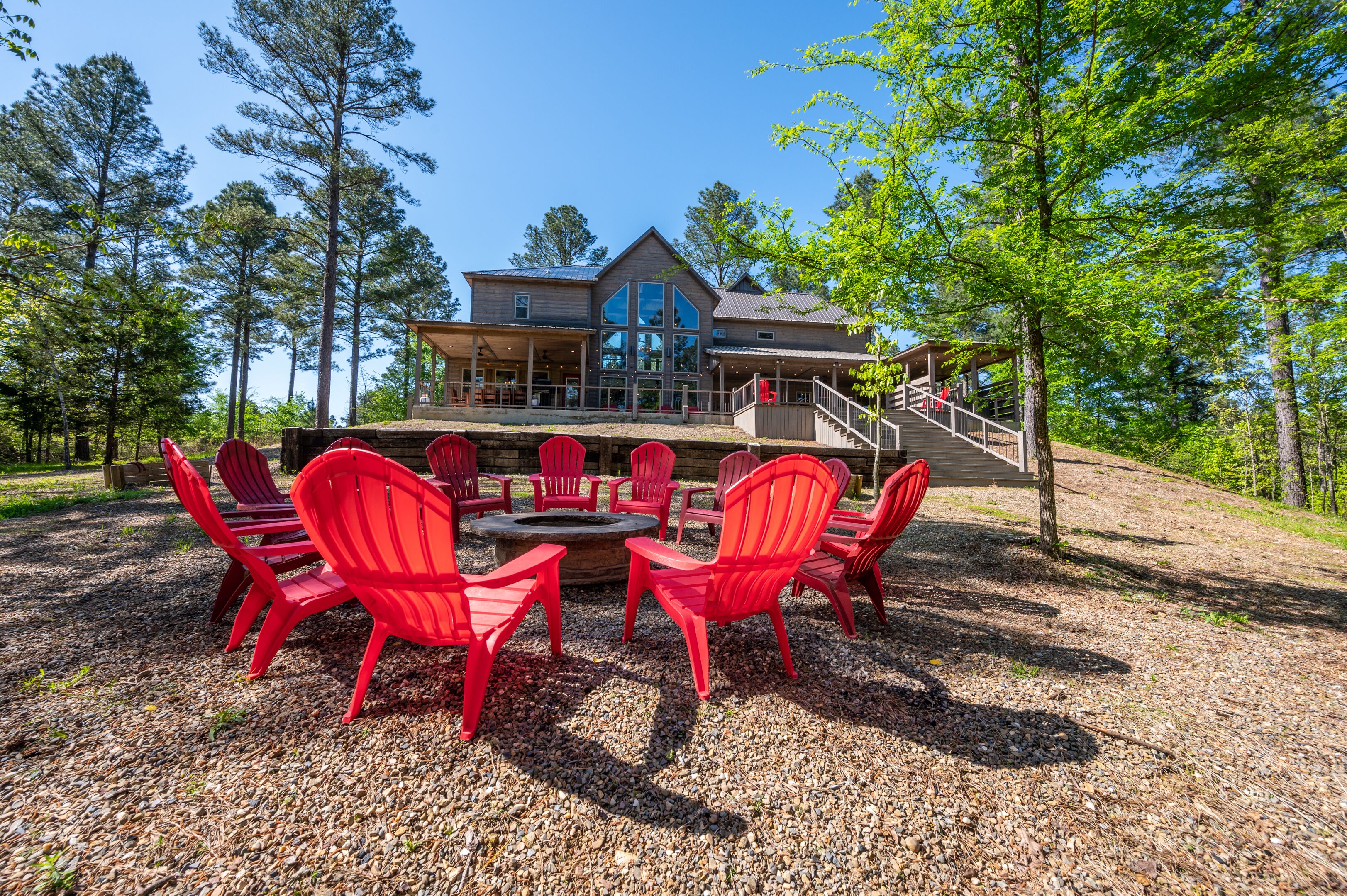Un chalet doté d’une grande terrasse, de chaises Adirondack rouges et d’un foyer en pierre.