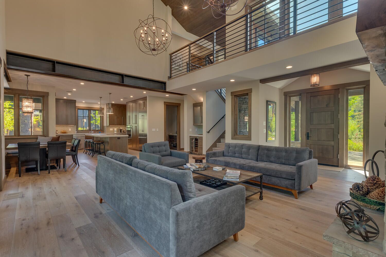 A spacious living room with a grey sofa set, a coffee table, and a dining area with a kitchen in the background.