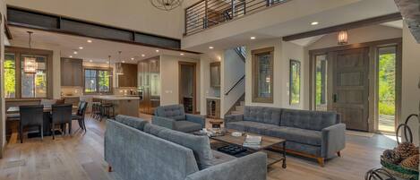 A spacious living room with a grey sofa set, a coffee table, and a dining area with a kitchen in the background.