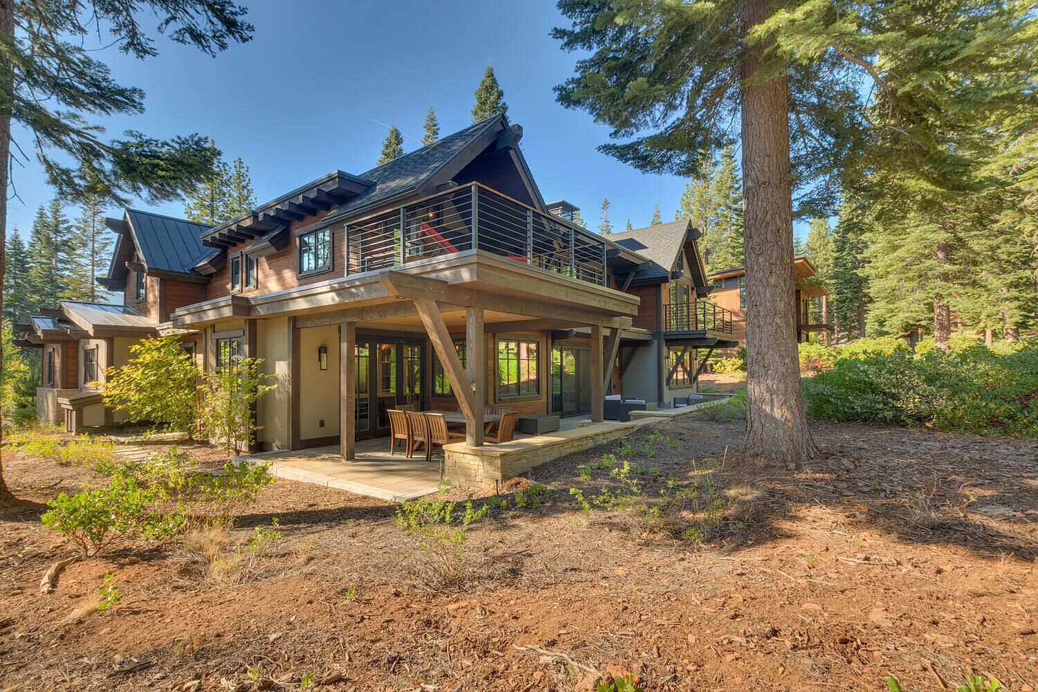 Una casa de dos pisos con un porche cubierto, ventanas amplias y vistas al bosque circundante.