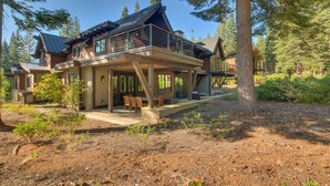 A two-story house with a covered patio, large windows, and a view of the surrounding forest.