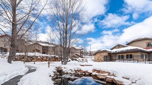 A snow-covered outdoor area with a pond, stone walls, and residential buildings. - Guest-Favorite Ski Home in Bear Hollow w/ Hot Tub – Sleeps 18 – King/Queen Beds (Park City)