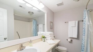 A bathroom with a sink, mirror, towel rack, toilet, and shower curtain.