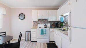 A compact kitchen with white cabinets, a stove, a sink, and a clock on the wall.