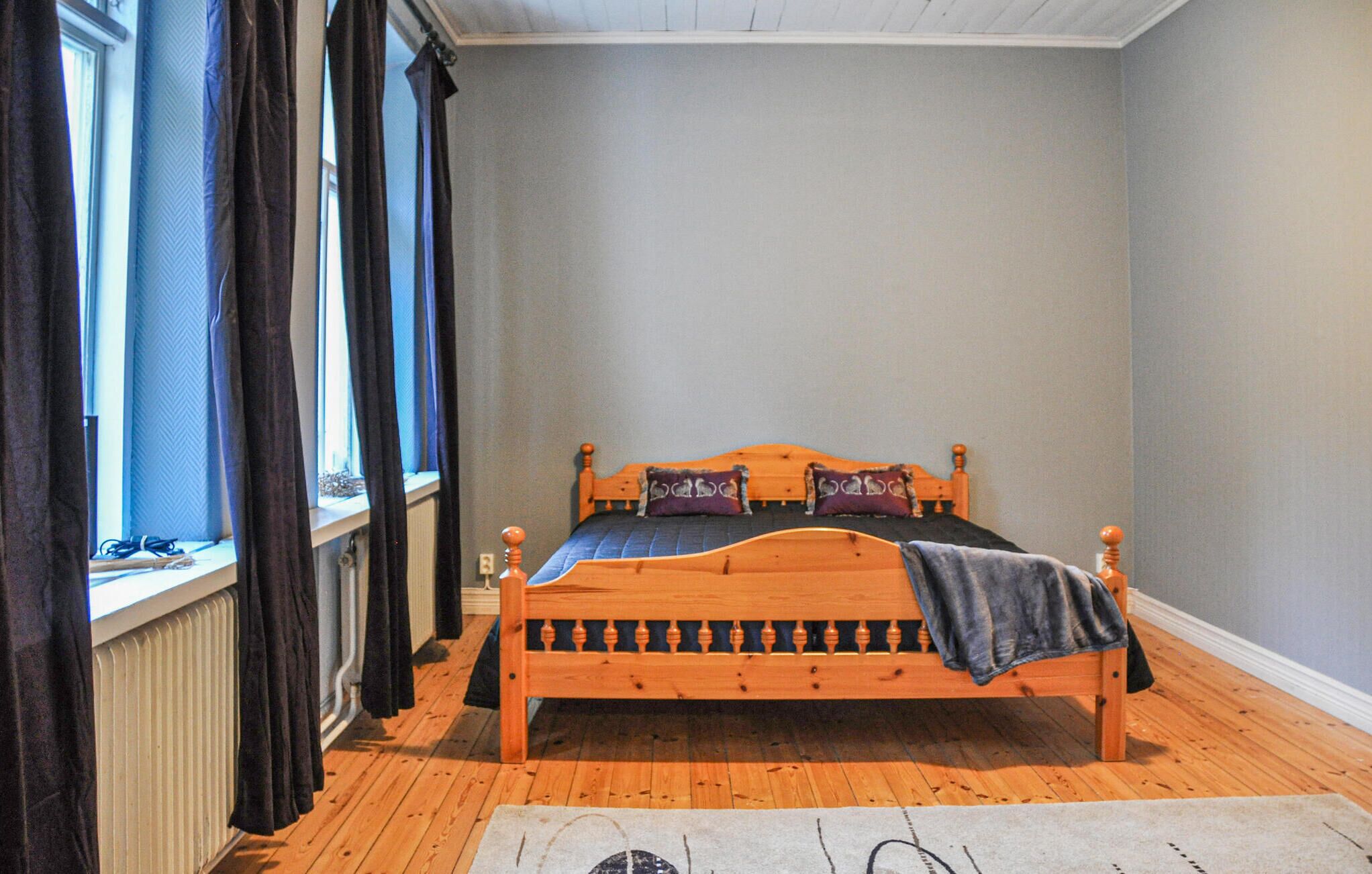 Une chambre avec un lit en bois, une fenêtre avec des rideaux et un radiateur.