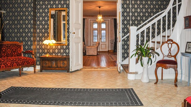 A spacious foyer with a patterned wallpaper, a wooden floor, a chandelier, a red armchair, a white door, and a staircase. - Stunning home in Värmlands Nysäter (Värmlands Nysäter)