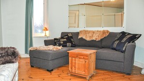 A living room with a grey sectional sofa, a small wooden chest of drawers, a fur throw, and a lamp by the window. - Stunning home in Värmlands Nysäter (Värmlands Nysäter)
