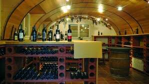 Une cave à vin avec des étagères et des barriques en bois, ainsi qu’une variété de bouteilles de vin.