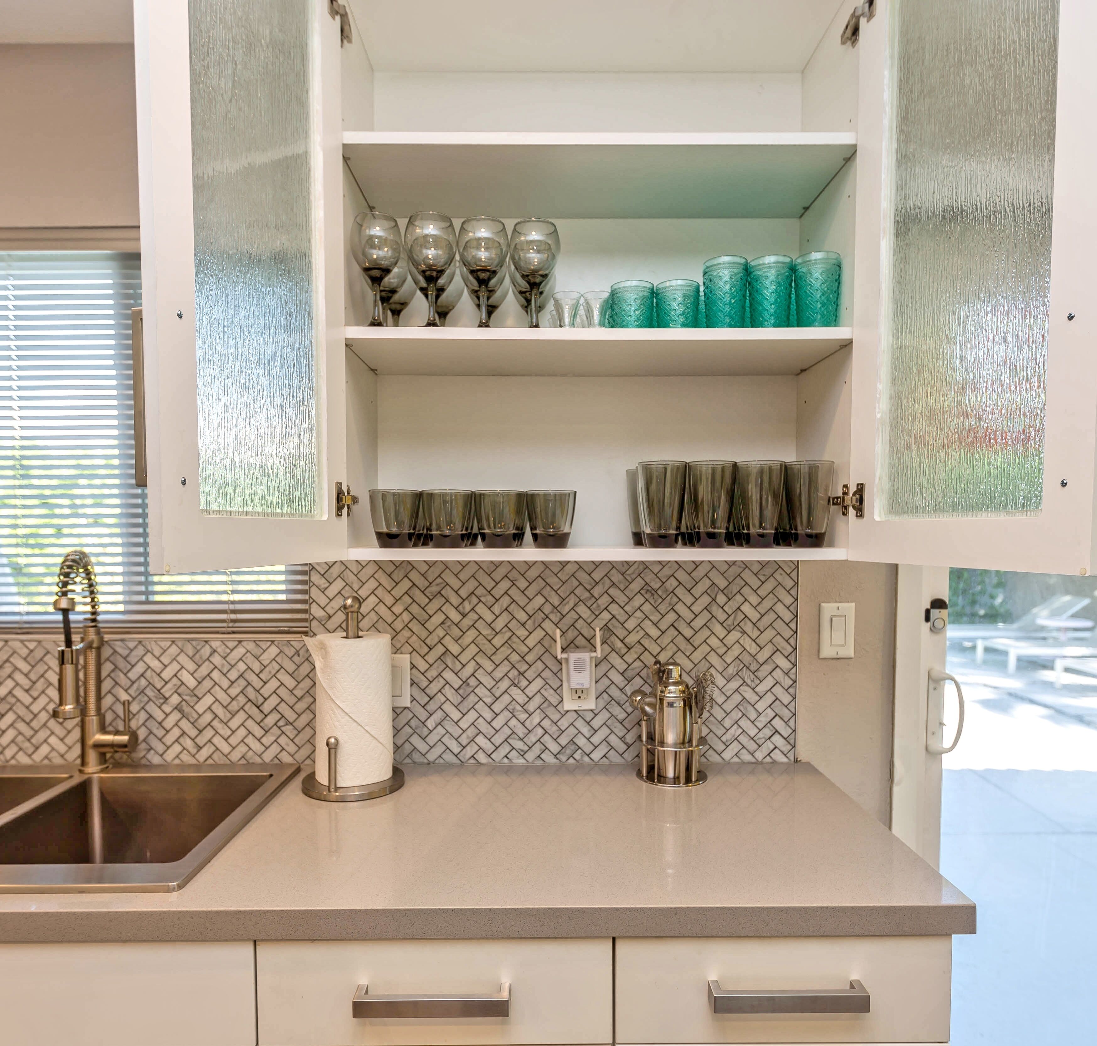 A kitchen with a herringbone tile backsplash, a stainless steel sink, and a paper towel holder.