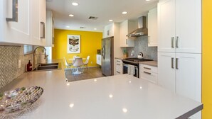 Une cuisine moderne avec des meubles blancs, un îlot central et un mur d’accent jaune.