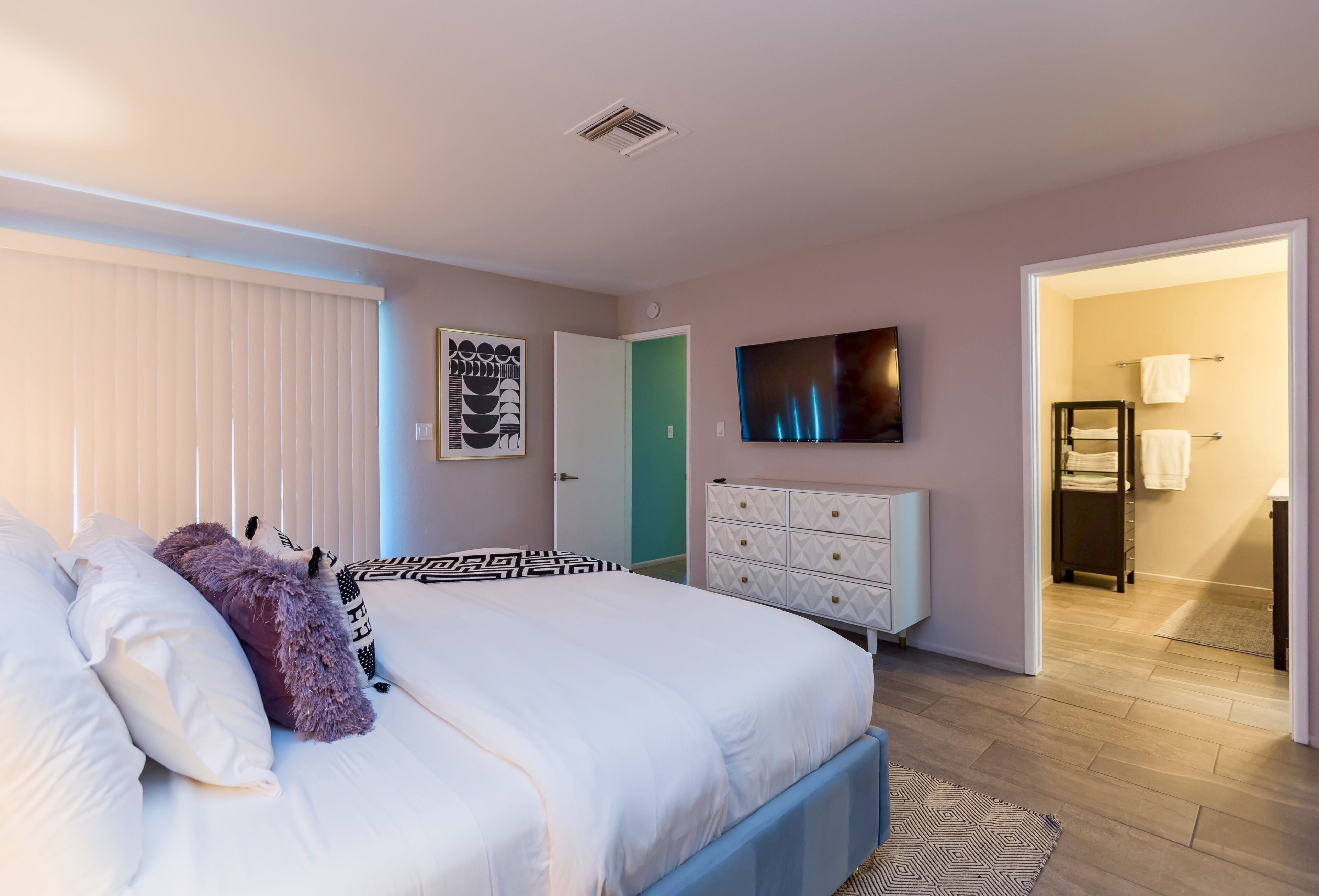 Ein Schlafzimmer mit Bett, Kommode, Fernseher und angrenzendem Badezimmer.