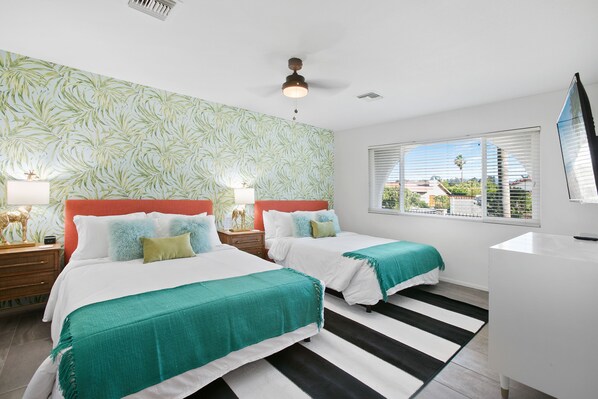 A hotel room with two beds, a large window with blinds, a ceiling fan, and a view of the outside.