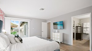 Une chambre avec un grand lit, une commode, une télévision et une vue sur l’extérieur.