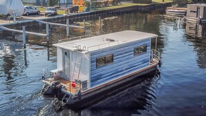 A houseboat with a covered deck, a small enclosed area with a ladder, and a water pump. - Cozy ship in Hennigsdorf with house sea view (Hennigsdorf)