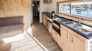 A modern kitchen with wooden cabinets, a built-in oven, a stove, and a large window overlooking a marina. - Cozy ship in Hennigsdorf with house sea view (Hennigsdorf)