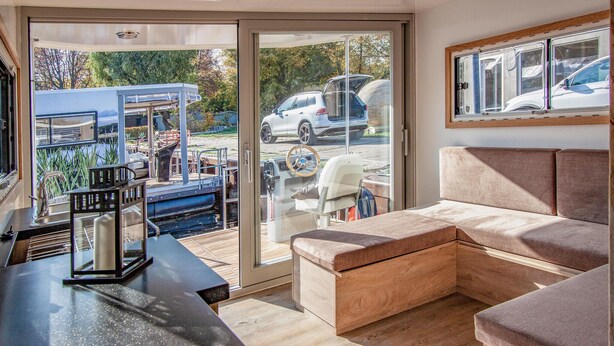 A modern living room with a sofa, a dining table, and a kitchen area with a sink and a stove. - Cozy ship in Hennigsdorf with house sea view (Hennigsdorf)
