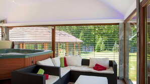 Un espace extérieur moderne, aménagé pour se détendre, avec un jacuzzi, des sièges confortables et une vue sur un paysage verdoyant.