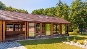 Une maison moderne dotée d’une grande extension en verre, de poutres en bois et d’un toit recouvert de tuiles.