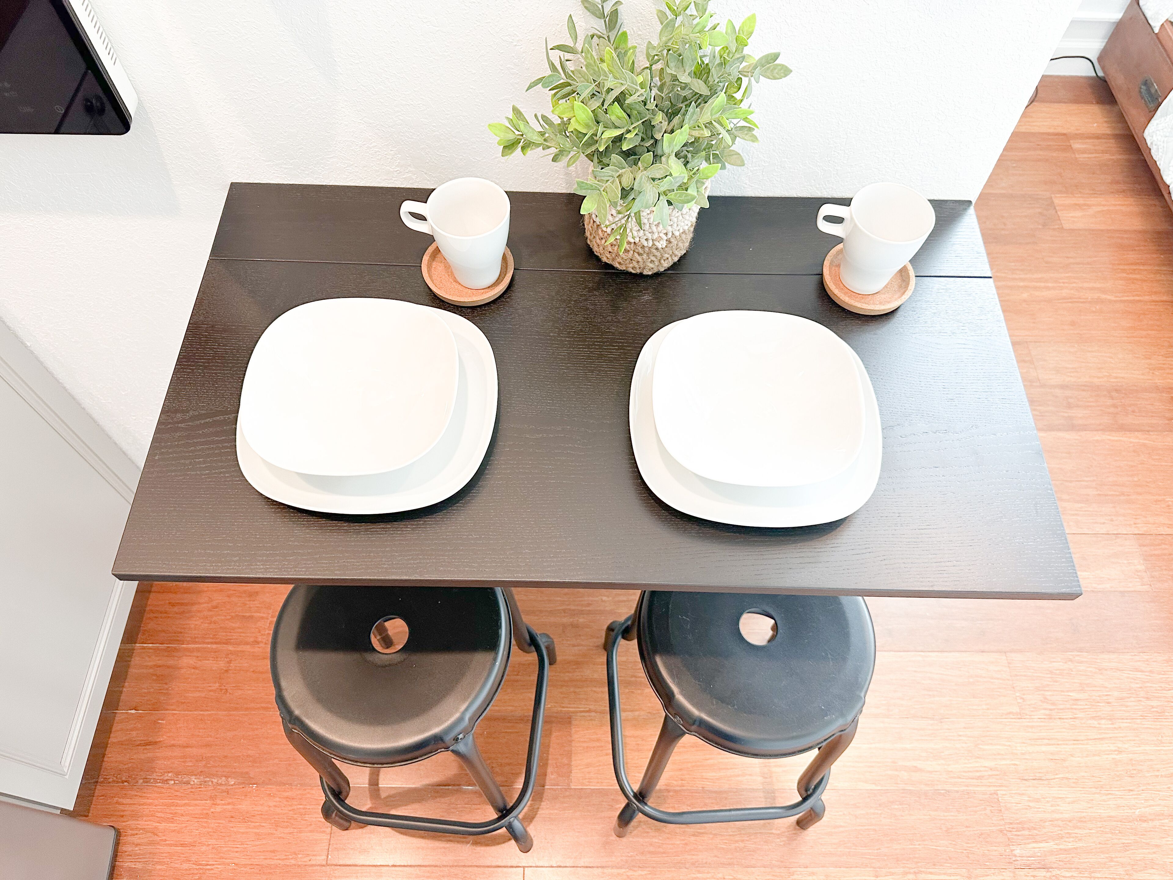 A dark wooden table with two white plates, two white cups, and a green plant.