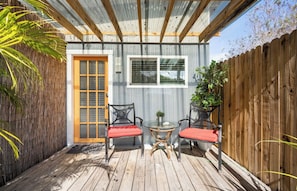 A small patio with two chairs and a table, a wooden door, and a window.