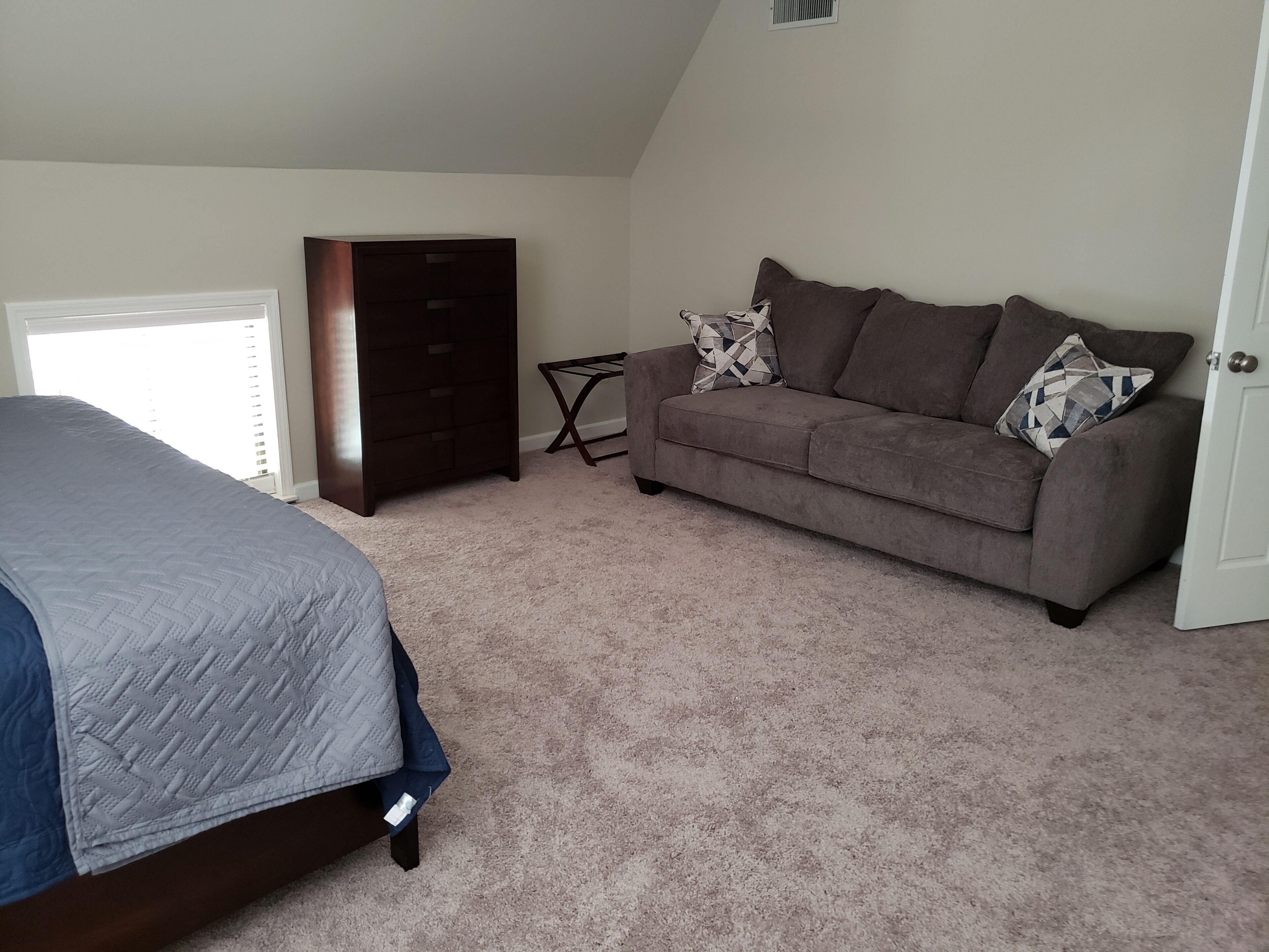 A bedroom with a bed, a dresser, a gray couch, and a door.