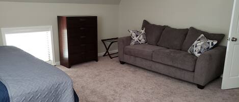 A bedroom with a bed, a dresser, a gray couch, and a door.