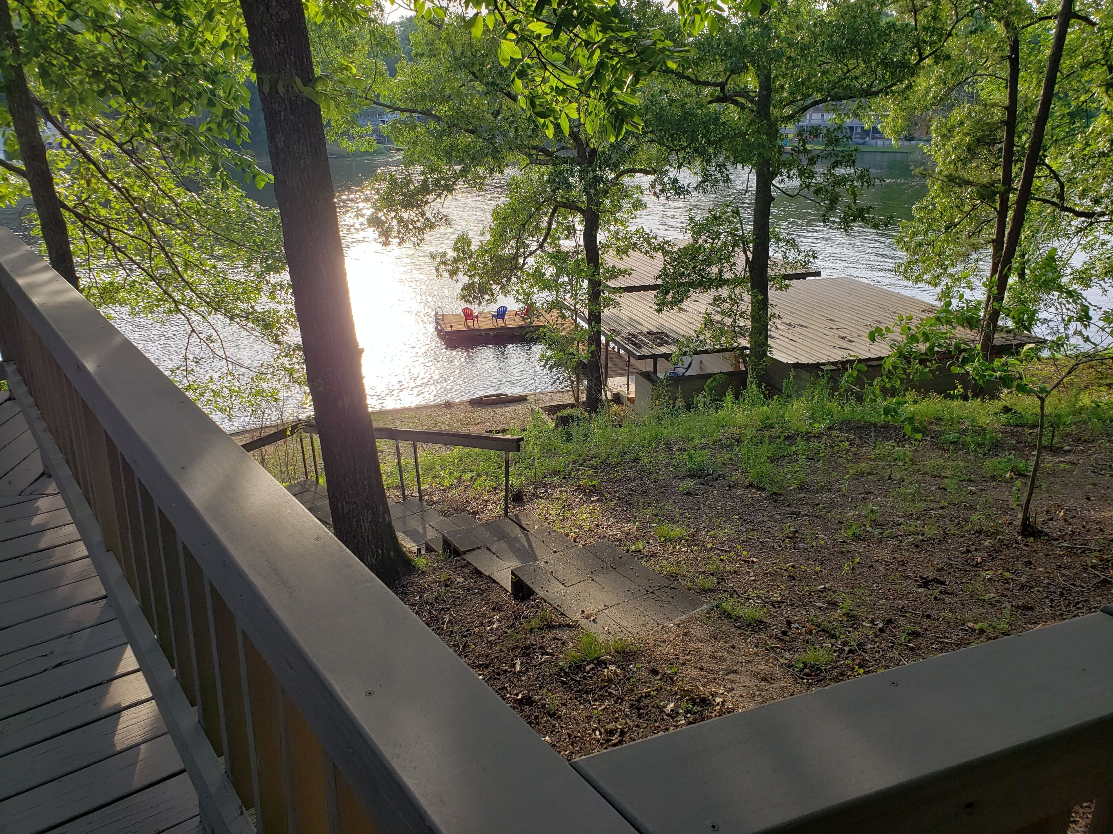 A wooden deck overlooking a calm lake with a dock and chairs.