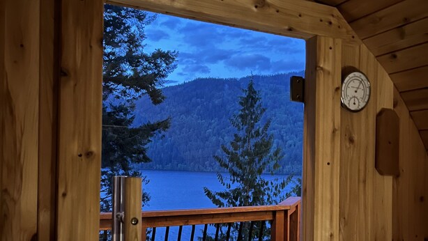 Een houten chalet met een balkon met uitzicht op een meer en beboste bergen.