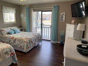Relax in this serene bedroom with a large bed, dresser, and wicker chair, offering a view of the outdoors through a sliding door.