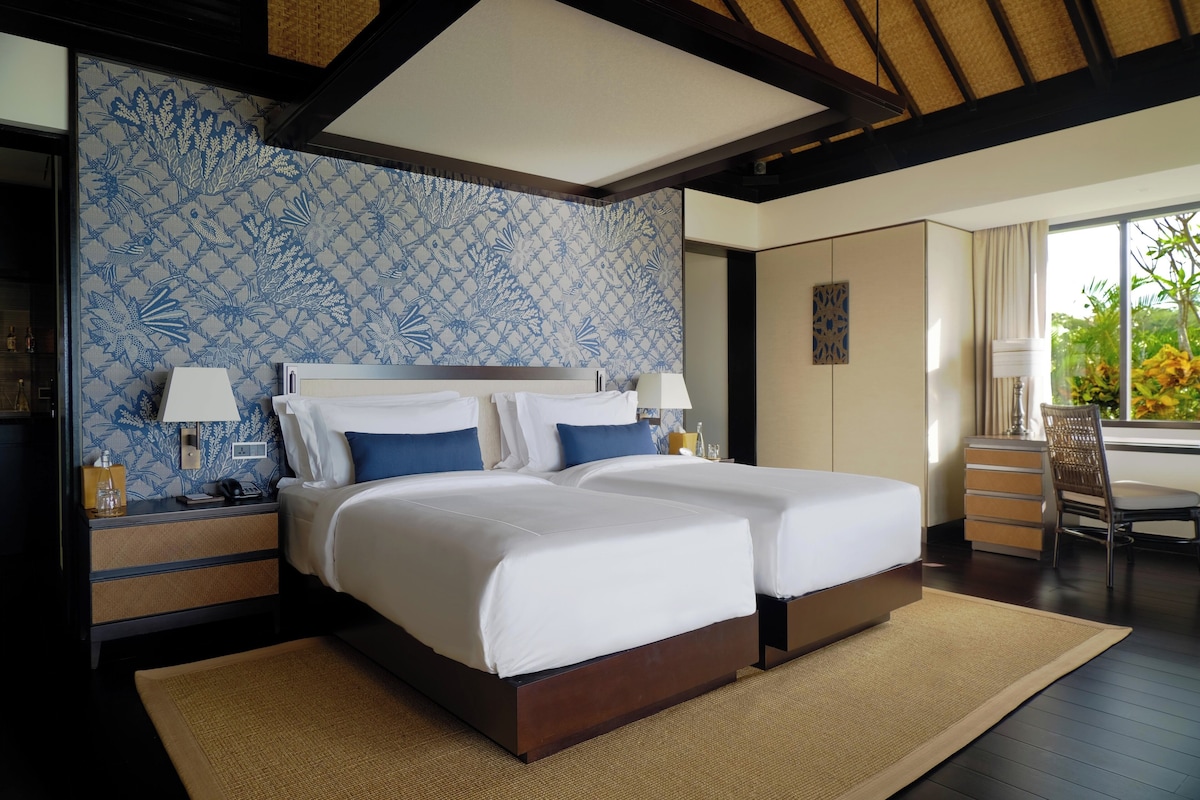 Habitación de hotel con dos camas, un ventanal con vistas a zonas verdes y una pared decorada.