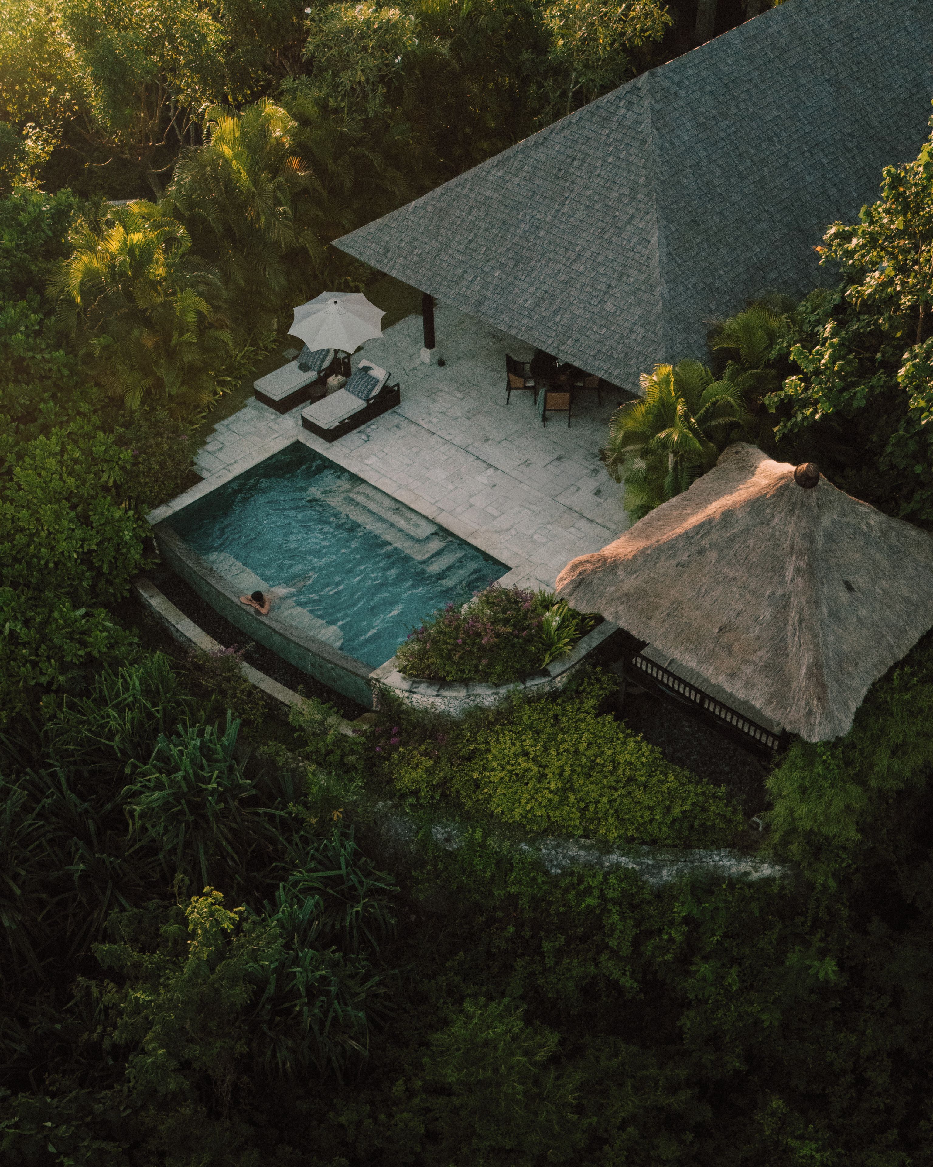 Vista aérea de una casa con piscina, sillas de descanso y una estructura de techo de paja.