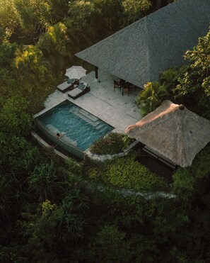 Vista aérea de uma casa com piscina, espreguiçadeiras e uma estrutura de telhado de palha.