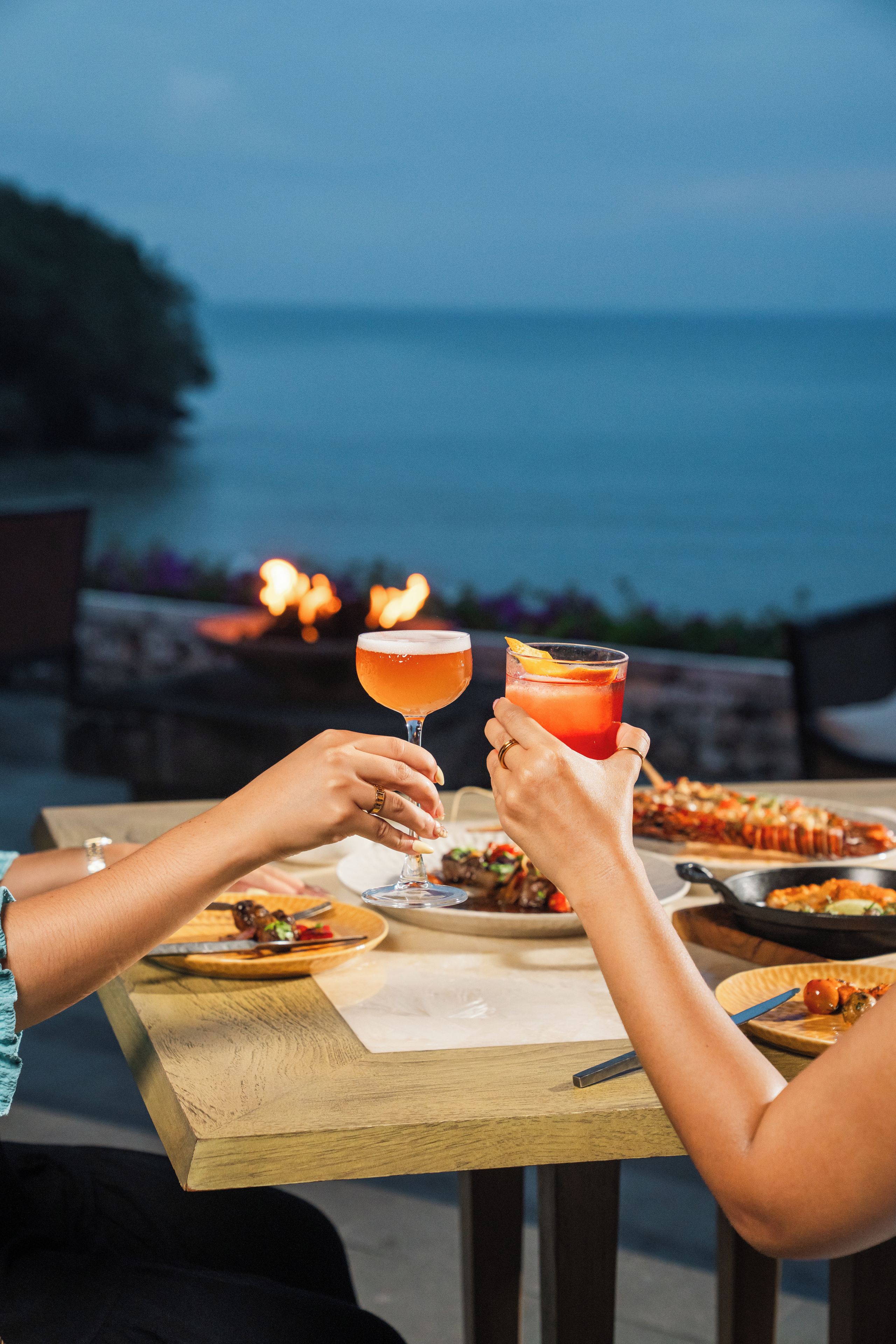 Dos personas brindando con bebidas en una mesa con vista al mar.