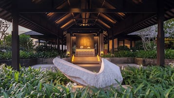 A covered outdoor area with a reception desk, plants, and a stone feature.