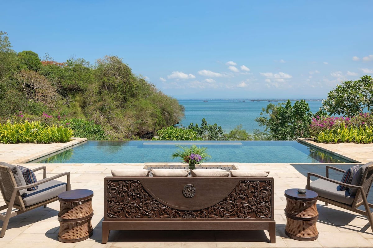 A poolside area with a view of the ocean, a lounge chair, a small table, and decorative plants.