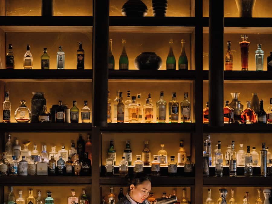 A bar with shelves of liquor bottles and a person preparing a drink.