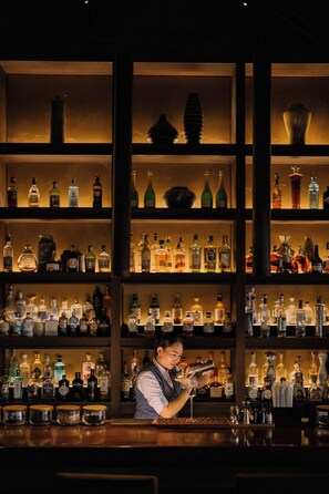 A bar with shelves of liquor bottles and a person preparing a drink. - Raffles Bali (Jimbaran)