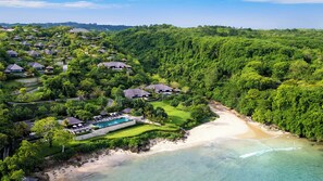 An aerial view of a resort with multiple bungalow-style buildings, a central pool area, and a beach. - Raffles Bali (Jimbaran)