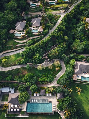 Luchtbeeld van een resort met meerdere zwembaden, kronkelende paden en weelderige begroeiing.