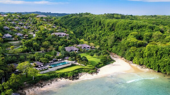 Vista aérea de um resort com várias construções semelhantes a bangalôs, uma área de piscina central e uma praia.