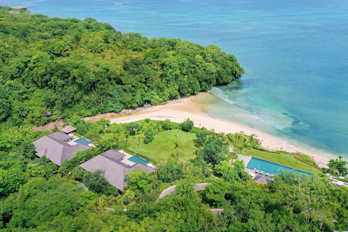 A tropical resort with a beach, swimming pool, and lush greenery.