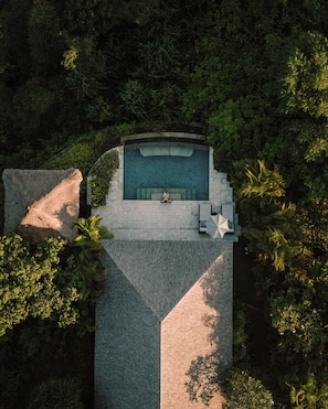 An aerial view of a swimming pool with a stone deck, surrounded by dense foliage. - Raffles Bali (Jimbaran)