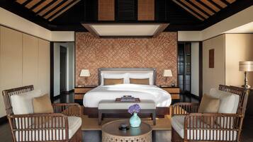 A hotel room with a large bed, two bedside tables, a round coffee table, and two wicker chairs.