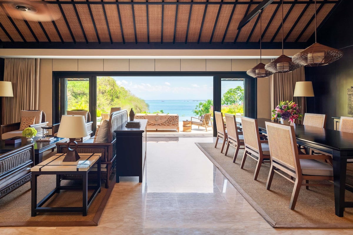 A spacious room with a view of the sea, a dining area with chairs and a table, and a seating area with sofas and a coffee table.