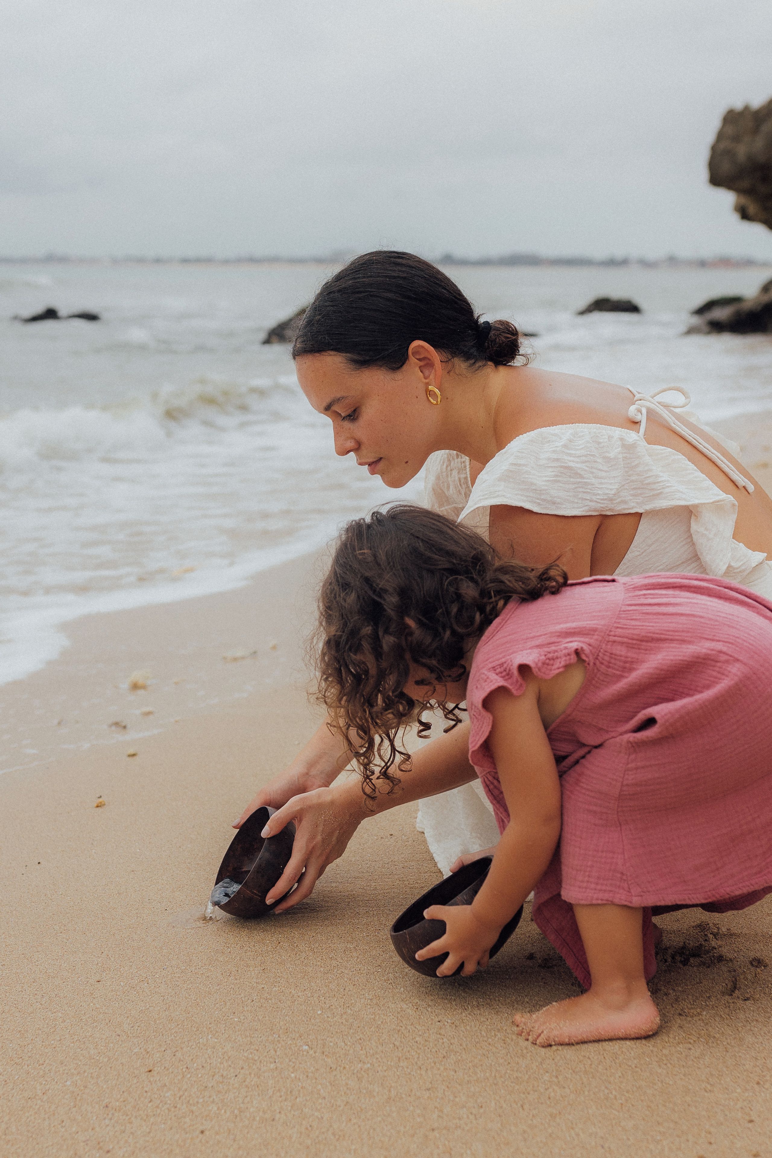 Escena de playa con una persona y un niño jugando con un recipiente.