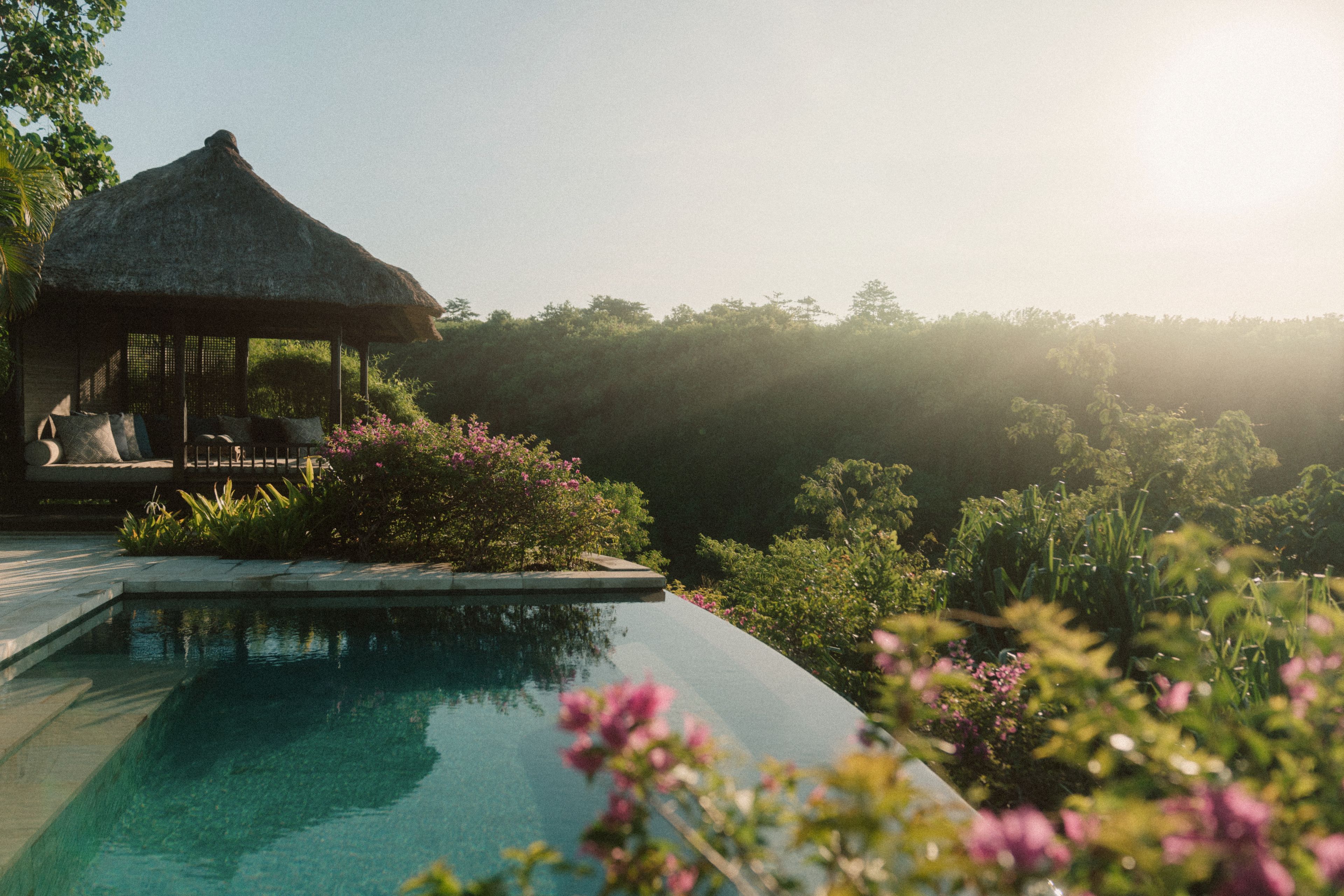 A pool with a thatched-roof structure and lounge chairs.